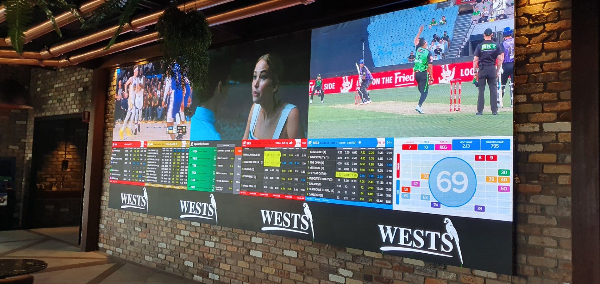 Multi-panel LED display wall at a Wests venue showing live sport, TAB wagering odds and keno alongside branded content.