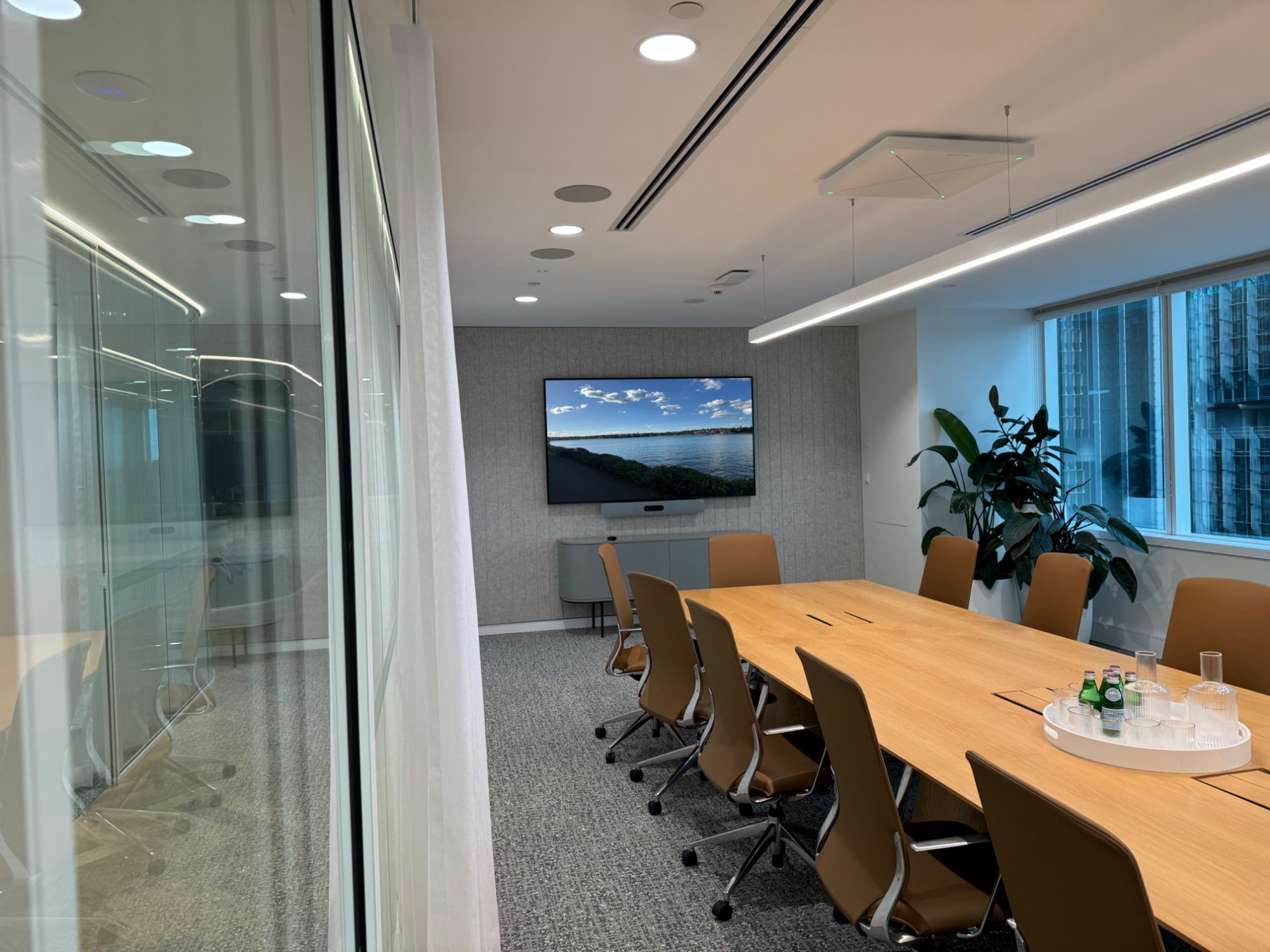 Boardroom video conferencing installation with a wall-mounted display, ceiling speakers and a discreet camera/mic bar.