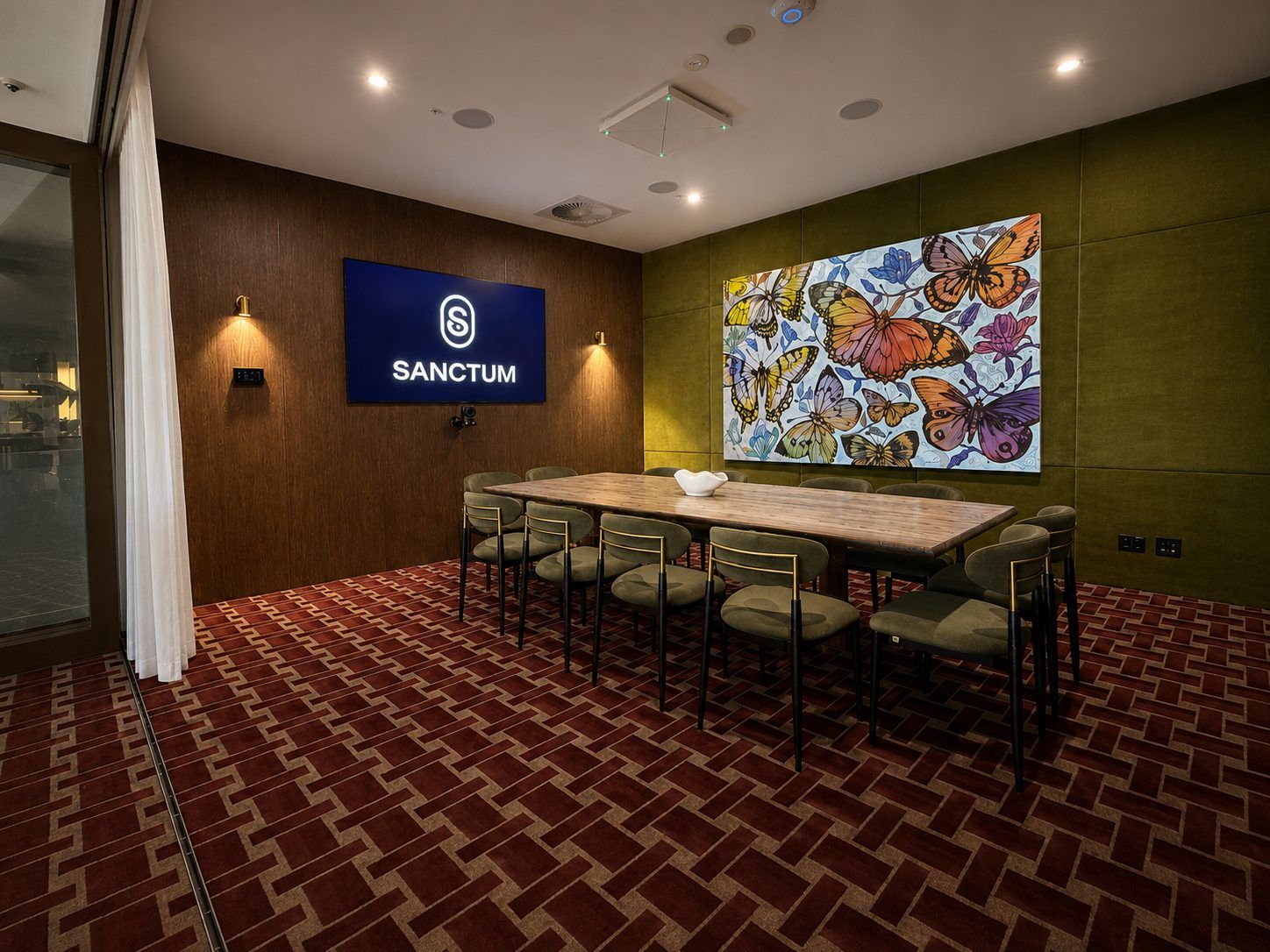 Wall-mounted video conferencing display and ceiling microphone/speaker in the Sanctum meeting room.