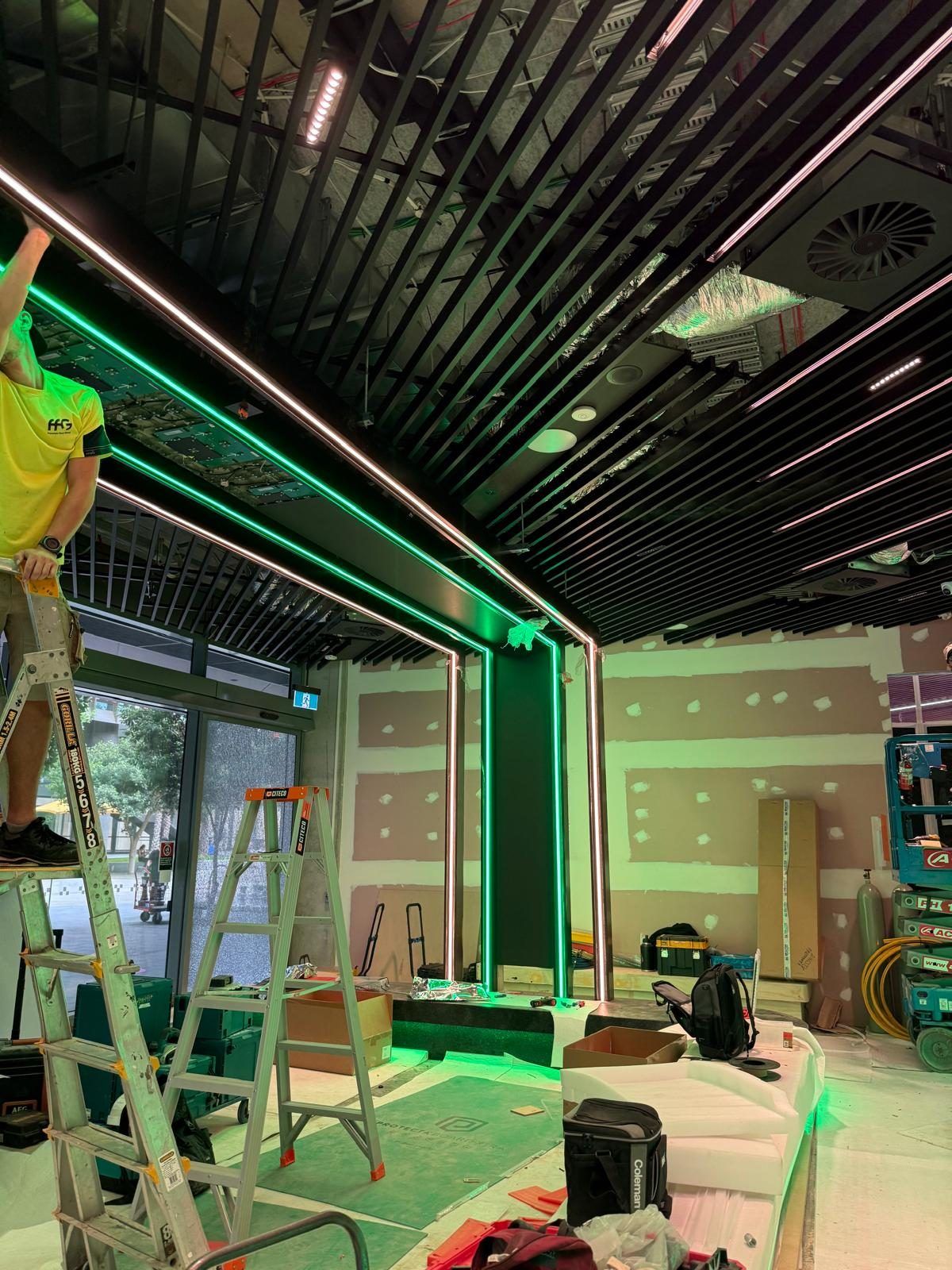 An installer completing the LED ribbon ceiling feature, with the strip lighting already live while the surrounding fit-out is finished around it.