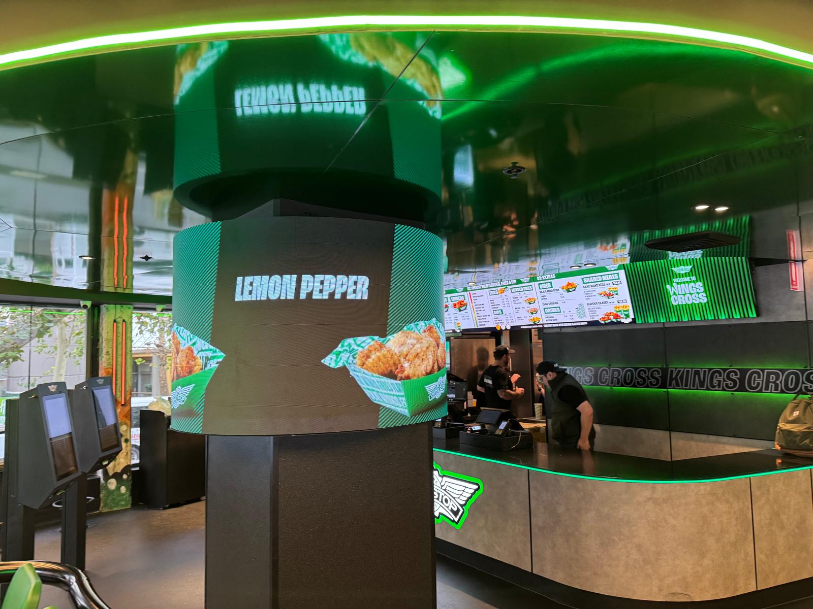 A finished curved LED column installation at a Wingstop store, displaying branded rotating menu content beside the servery counter.